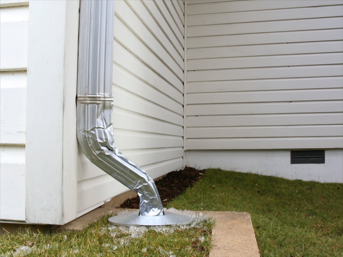 Aluminum downspout on a sided house after a hailstorm, with ice pellets on the grass